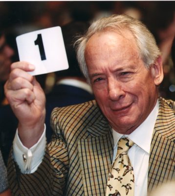 Person in checkered suit holding a card with the number 1 in a blurred indoor setting.