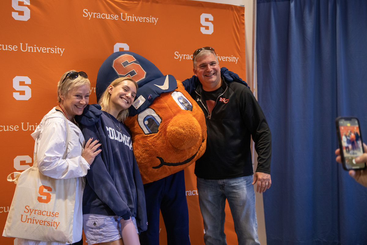 Two women and a man posing for a photo with Otto the Orange.