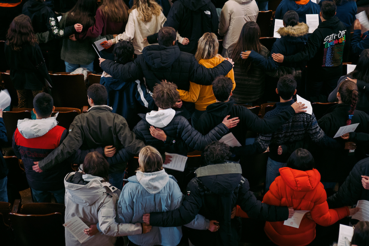 Ground of students standing together with their backs to the camera linking arm and arm.
