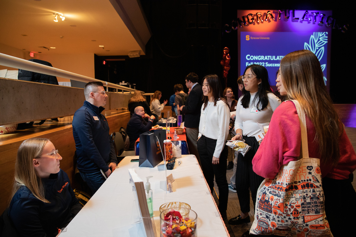 Several students standing at a table talking to two individuals 