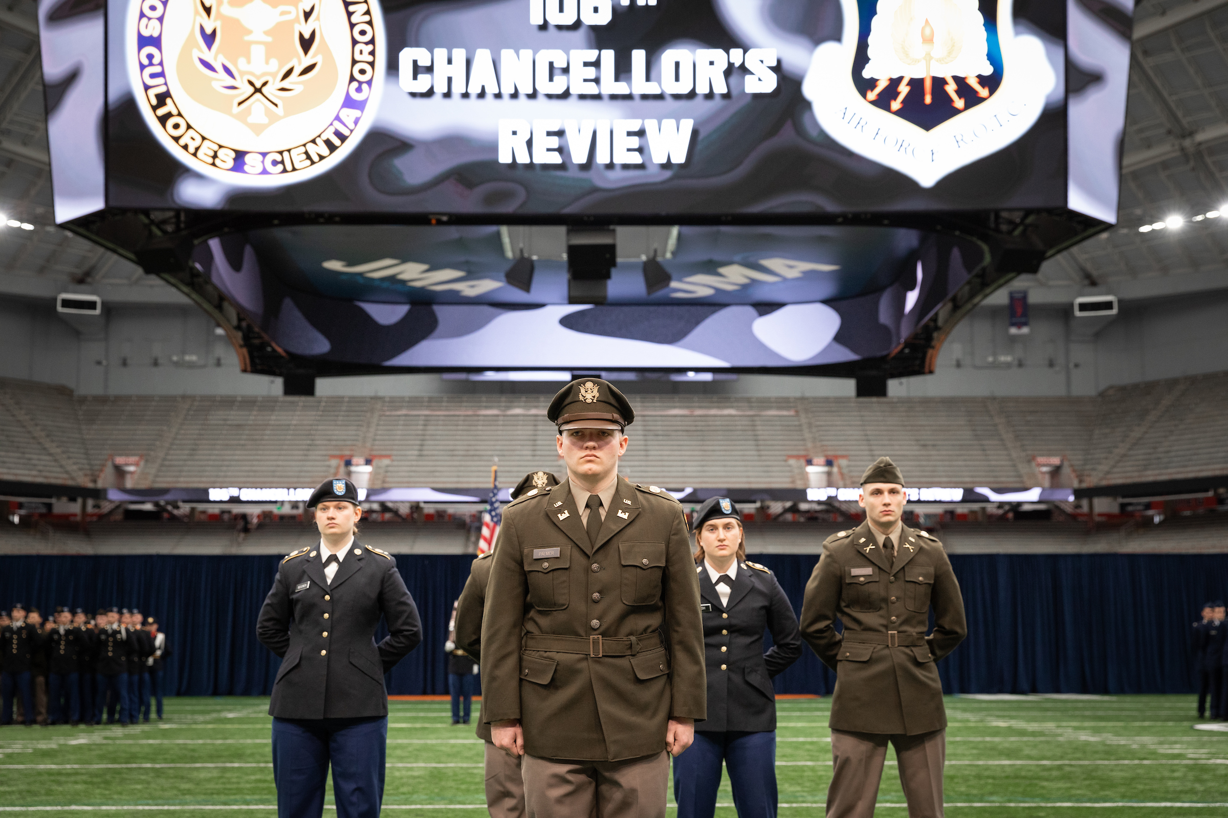 Small group of individuals standing in formation in military uniforms on the field in the JMA Wireless Dome