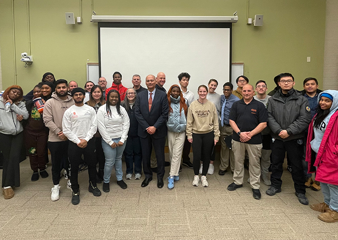 Large group of people standing together in classroom.