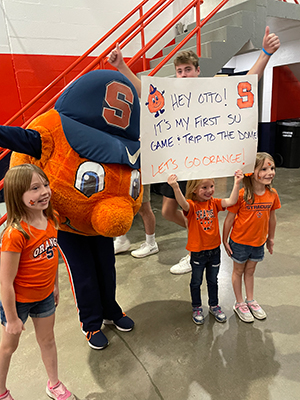 Otto standing with little kids in orange tshirts holding a poster sign