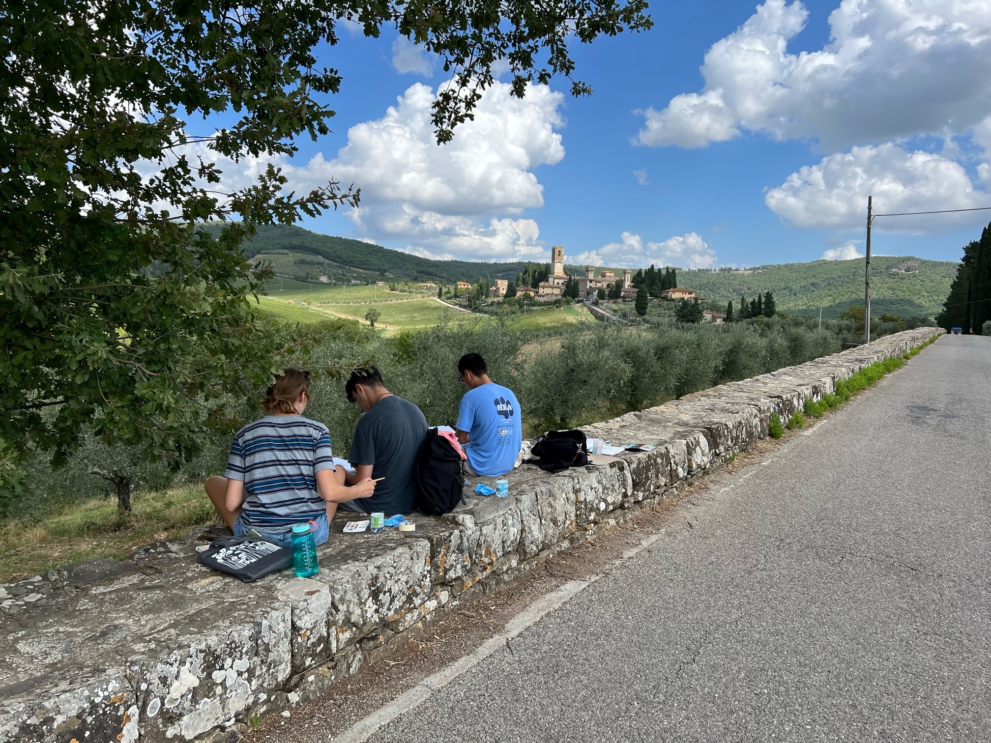 Three individuals sitting on a wall painting with a beautiful stone castle looking building off in the distance.