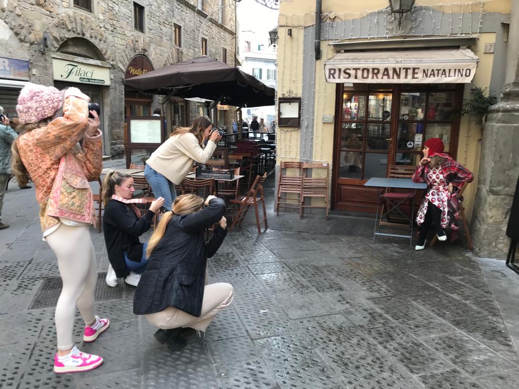 Four individuals taking a photo of another individual sitting at a table posing for the photo. 