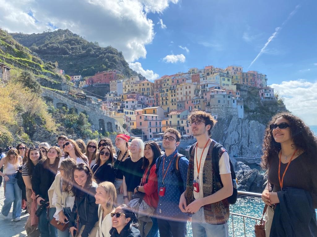 Group of individuals standing together with a mountain side in the background with multi-colored buildings all situated together.