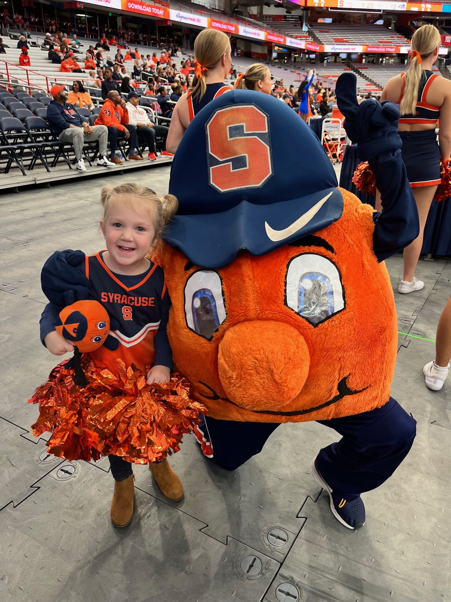 Small child holding pom poms standing next to Otto the Orange