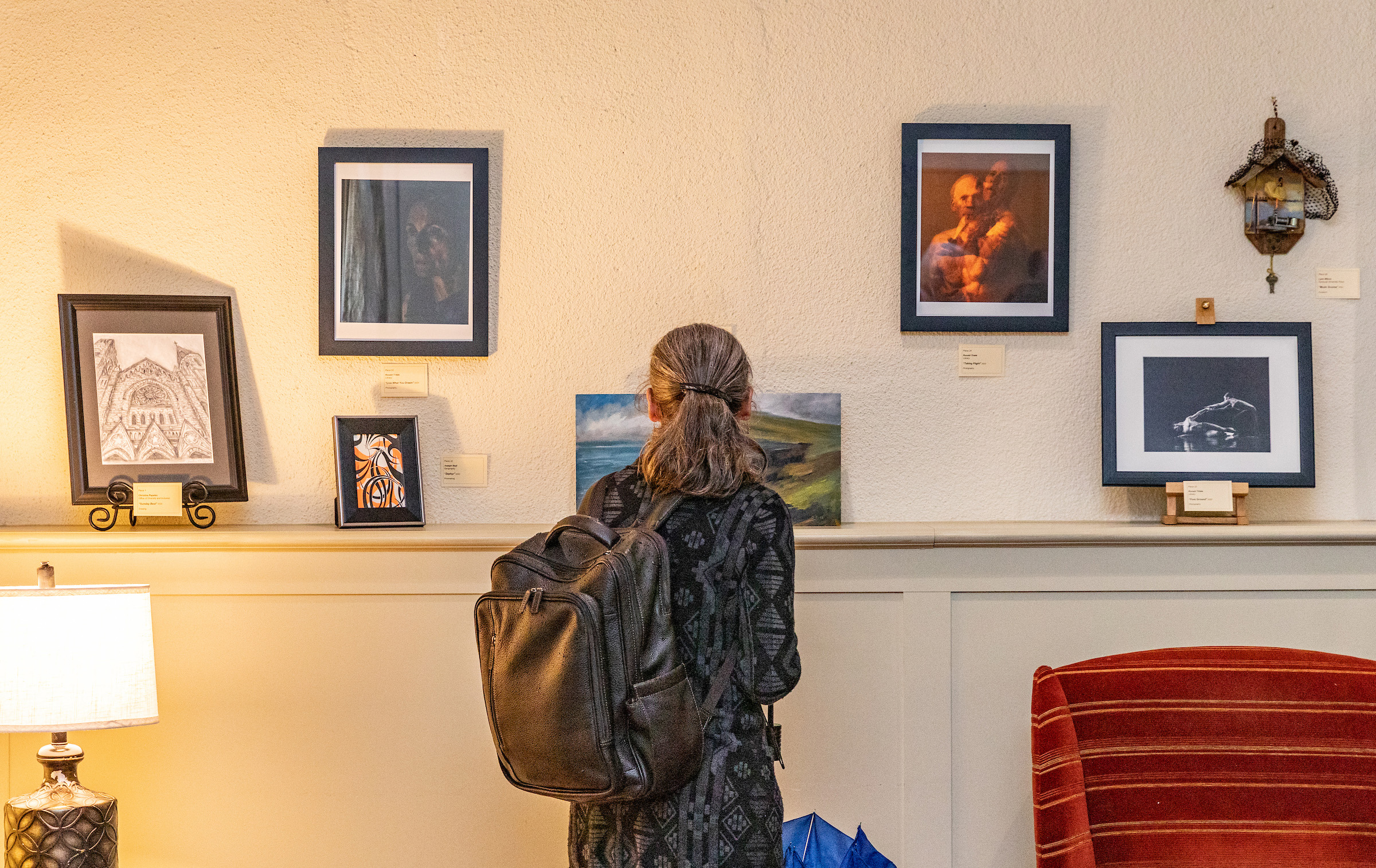Individual looking at various artwork pieces on a white wall.