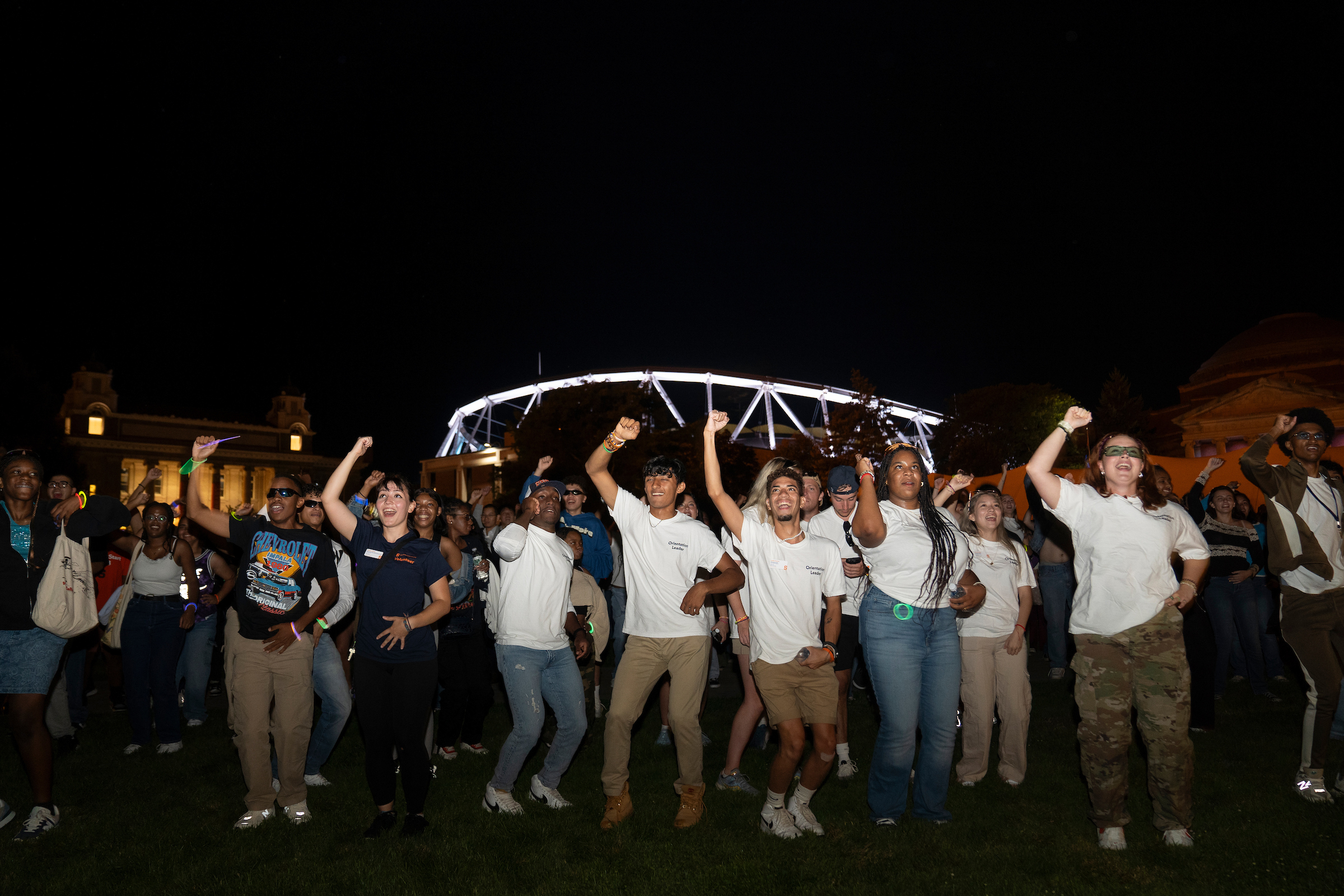 Large group of students dancing outside at night time