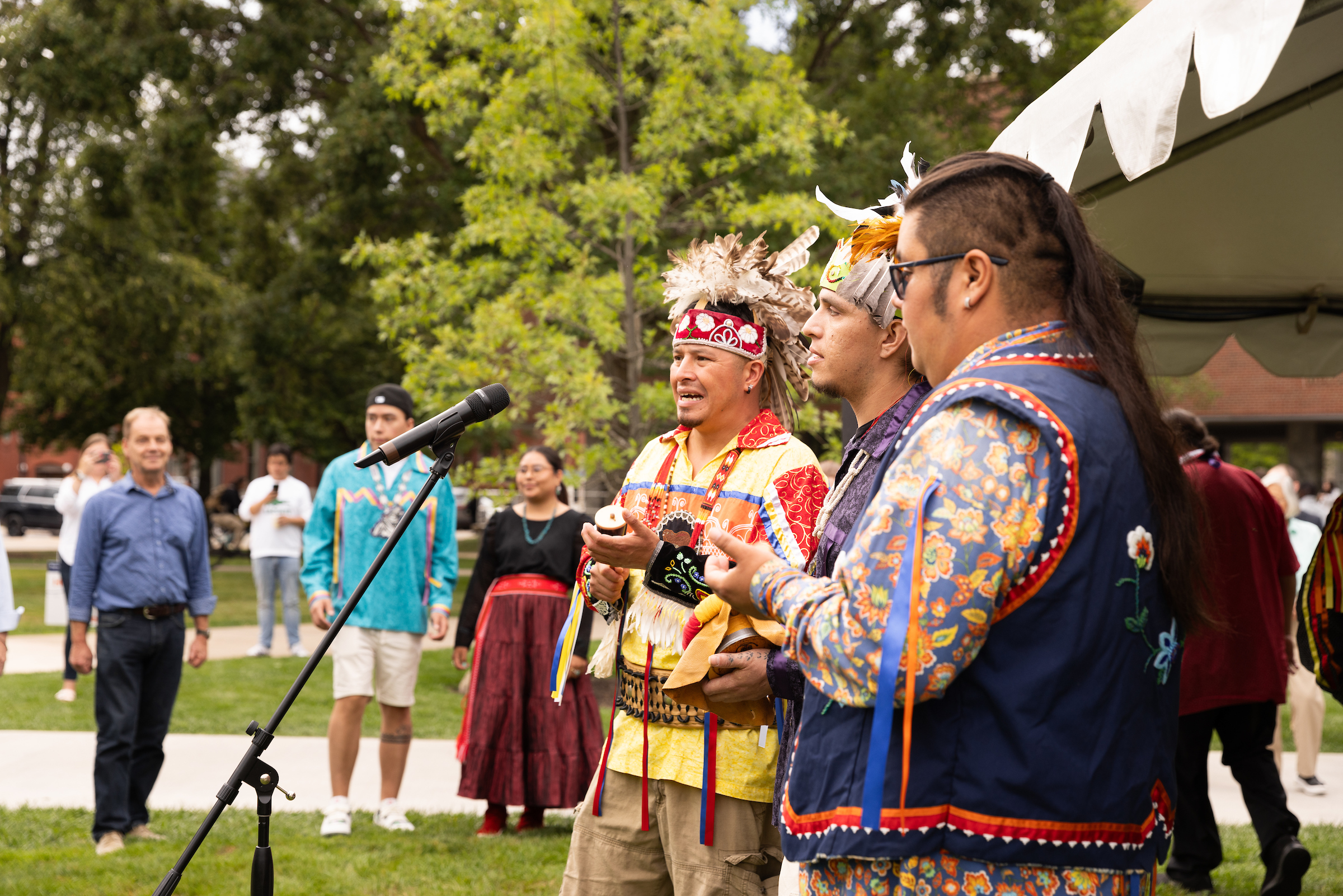 Three individuals playing instruments to those gathered at the 2023 Haundenosaunee Welcome Gathering