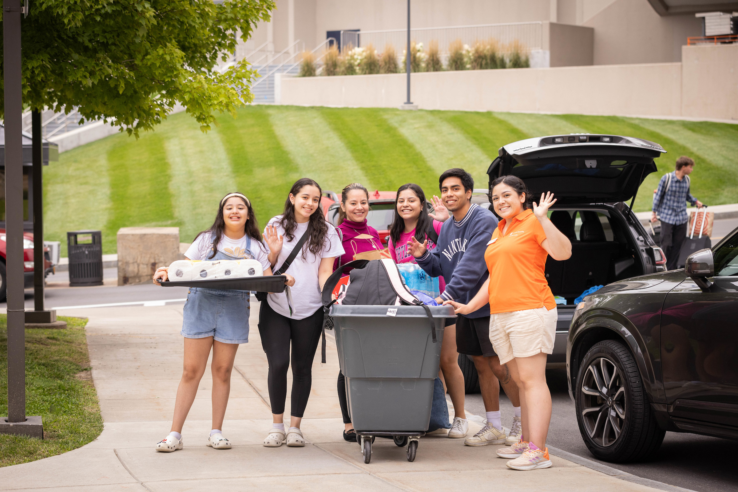 Group of people standing together on the sidewalk with a grey bin and holding other items to move in