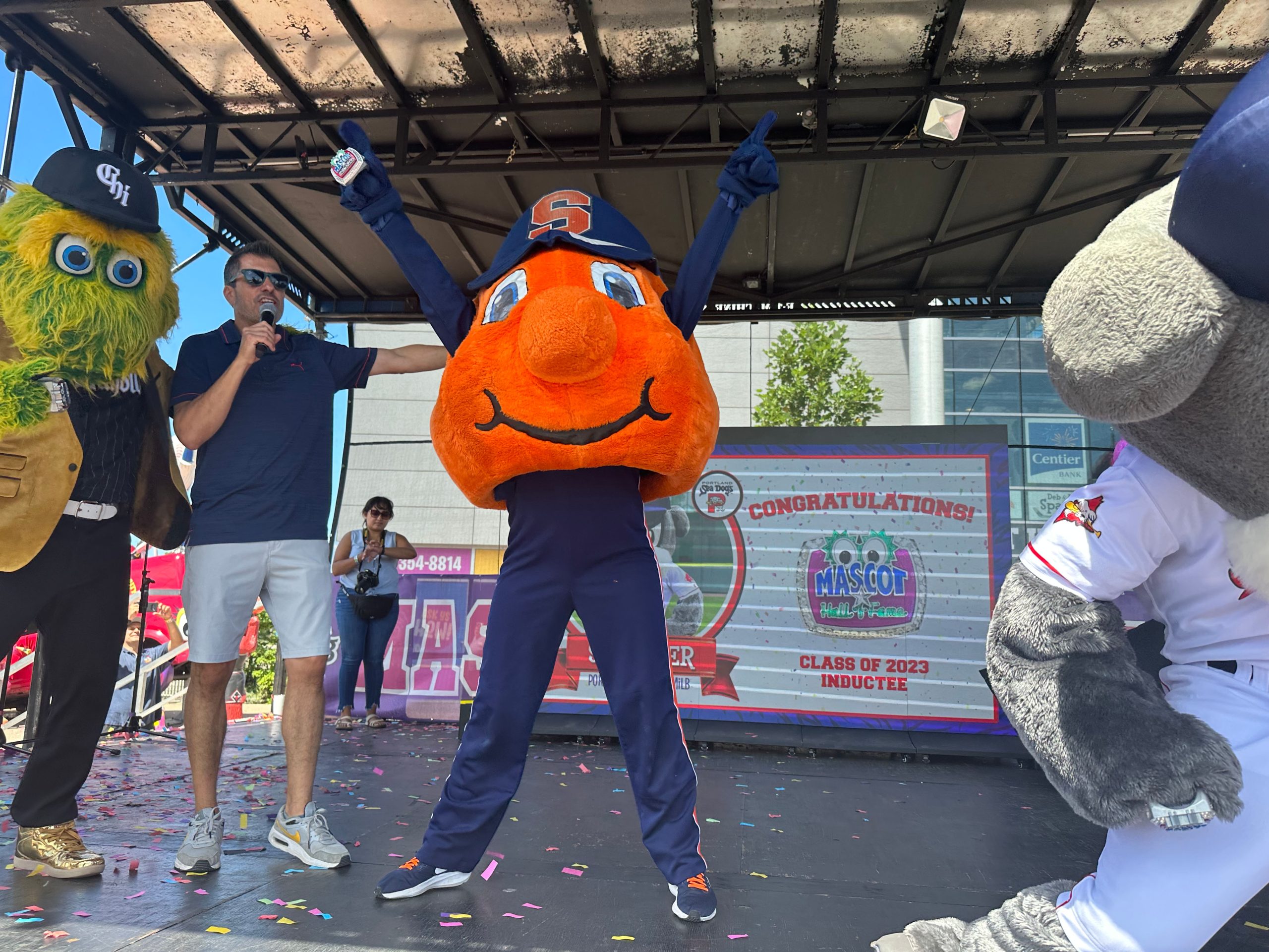 Otto the Orange standing on stage with their Hall of Fame ring. 