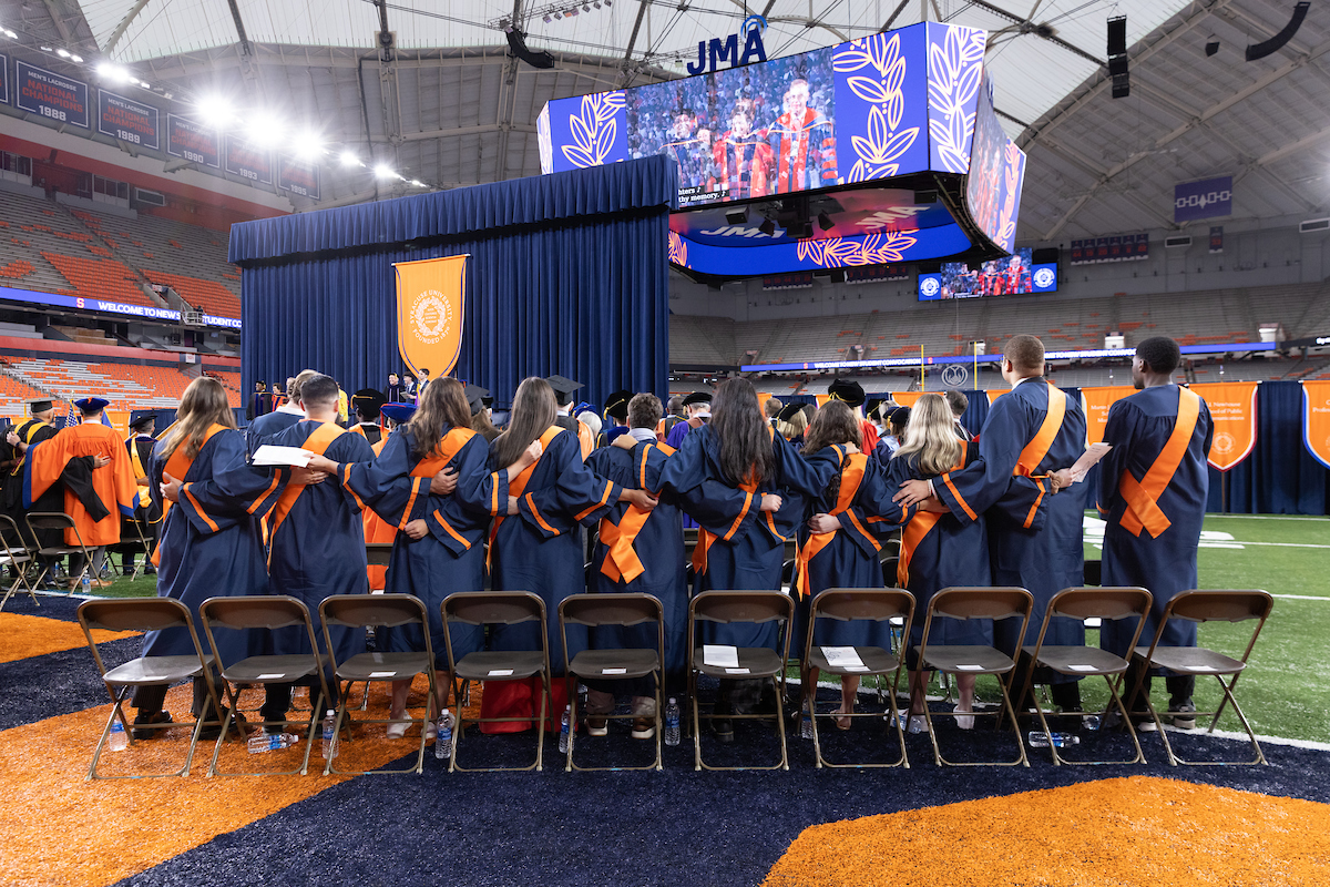 Shot from behind of students standing up and swaying to the alma mater at new student convocation