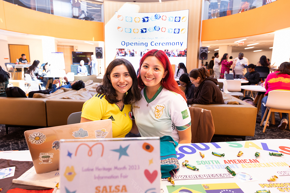 Two students sitting at an information table in the Schine student center
