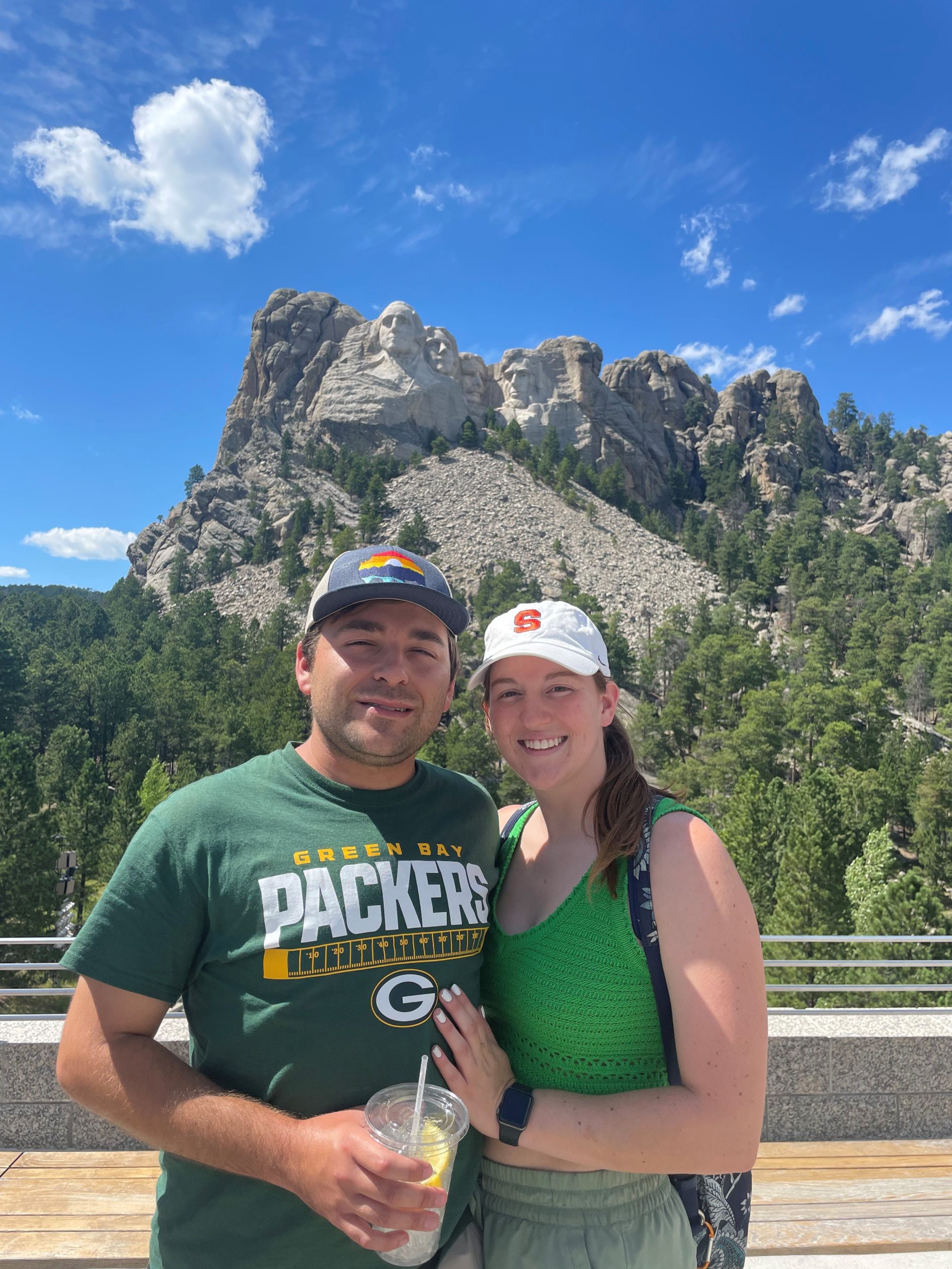 Two individuals standing in front of Mt. Rushmore on a sunny day.