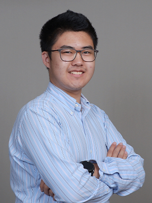 undergraduate student Yida He poses with his arms across in front of a studio backdrop