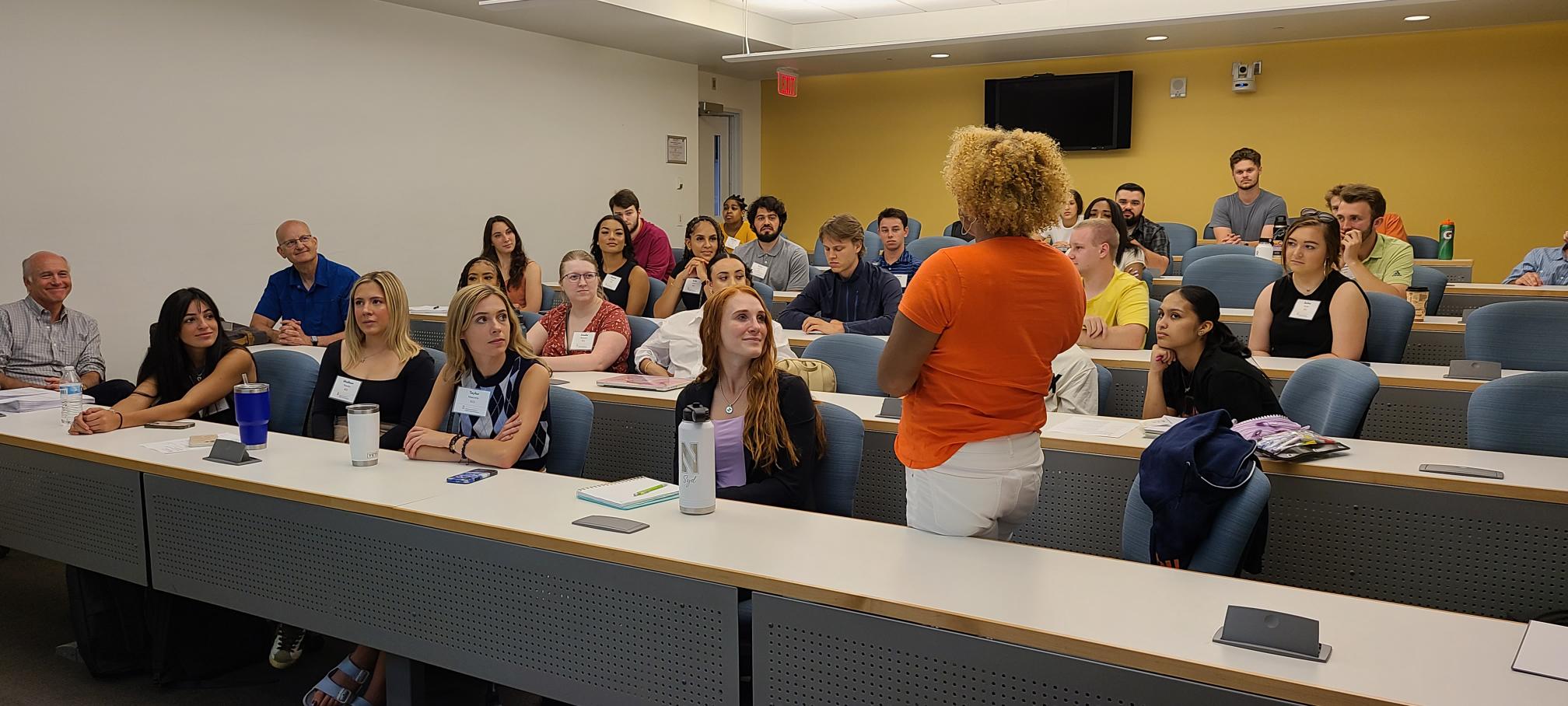 One student standing and talking to a group of students sitting in a classroom