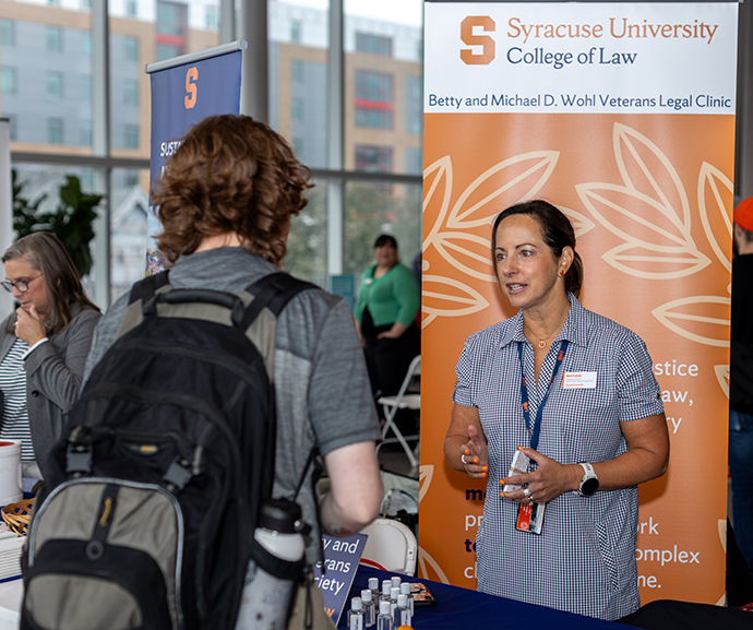 Woman standing at a table talking to a student with a backpack on.