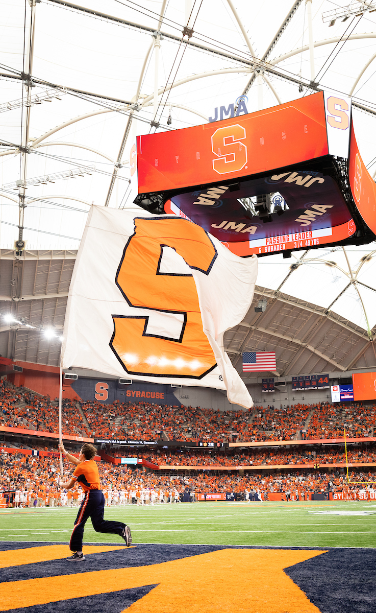 Student running with a large white and orange S flag on the field during a game in the Dome. 