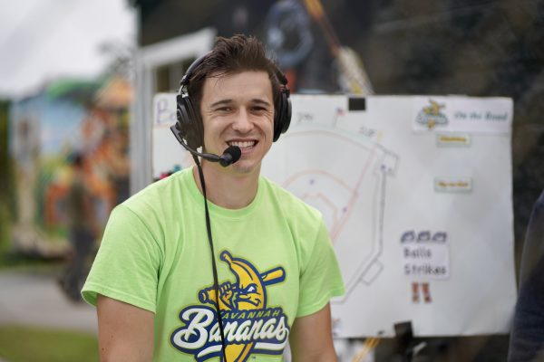 A man calls a Savannah Bananas baseball game while wearing a lime green Bananas t-shirt.