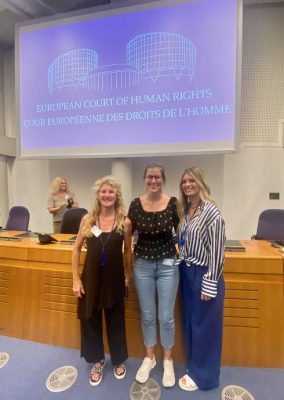 three individuals stand in front of a projector screen at the European Court of Human Rights