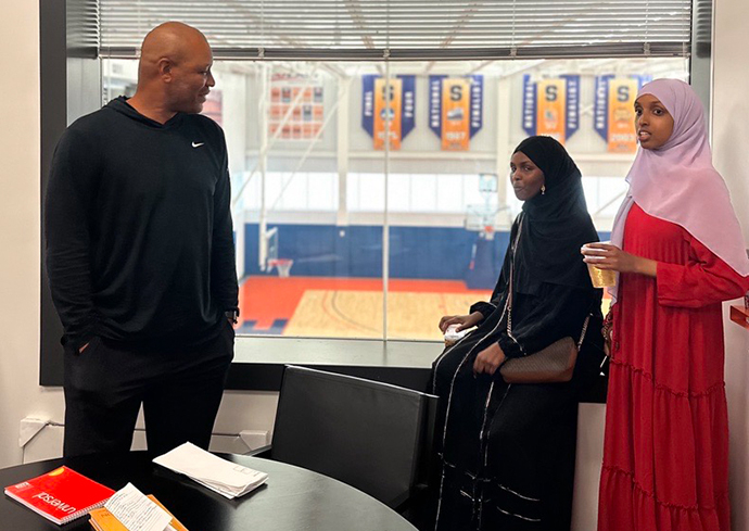 Two students with Coach Autry in his office overlooking the practice basketball court