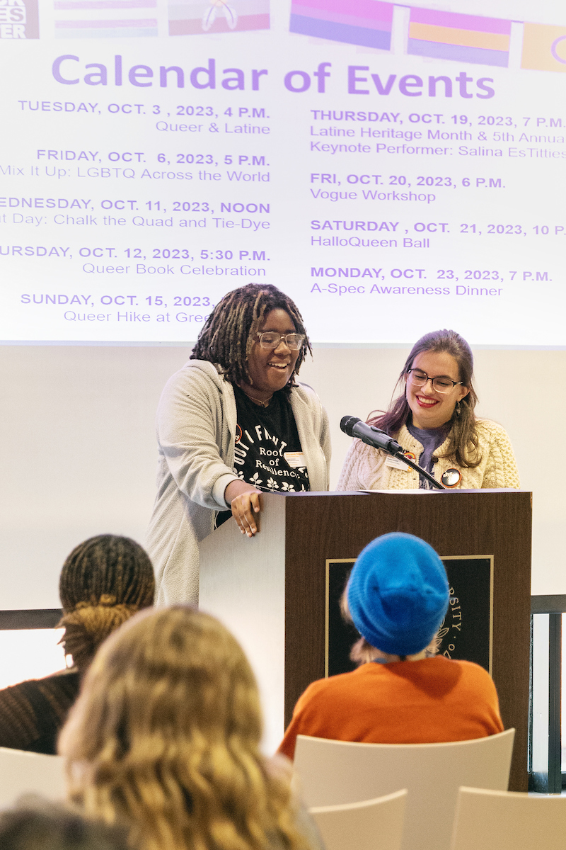 Two individuals standing at a podium speaking to an audience. 