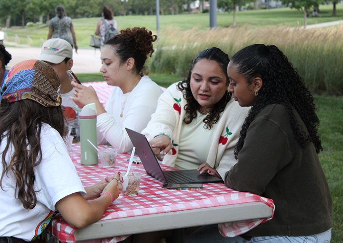 Group of students sitting at a table eating ice cream and looking at a laptop computer.