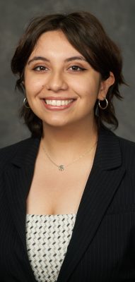 A woman smiles for a headshot while wearing a black sport coat and a polka dot blouse.