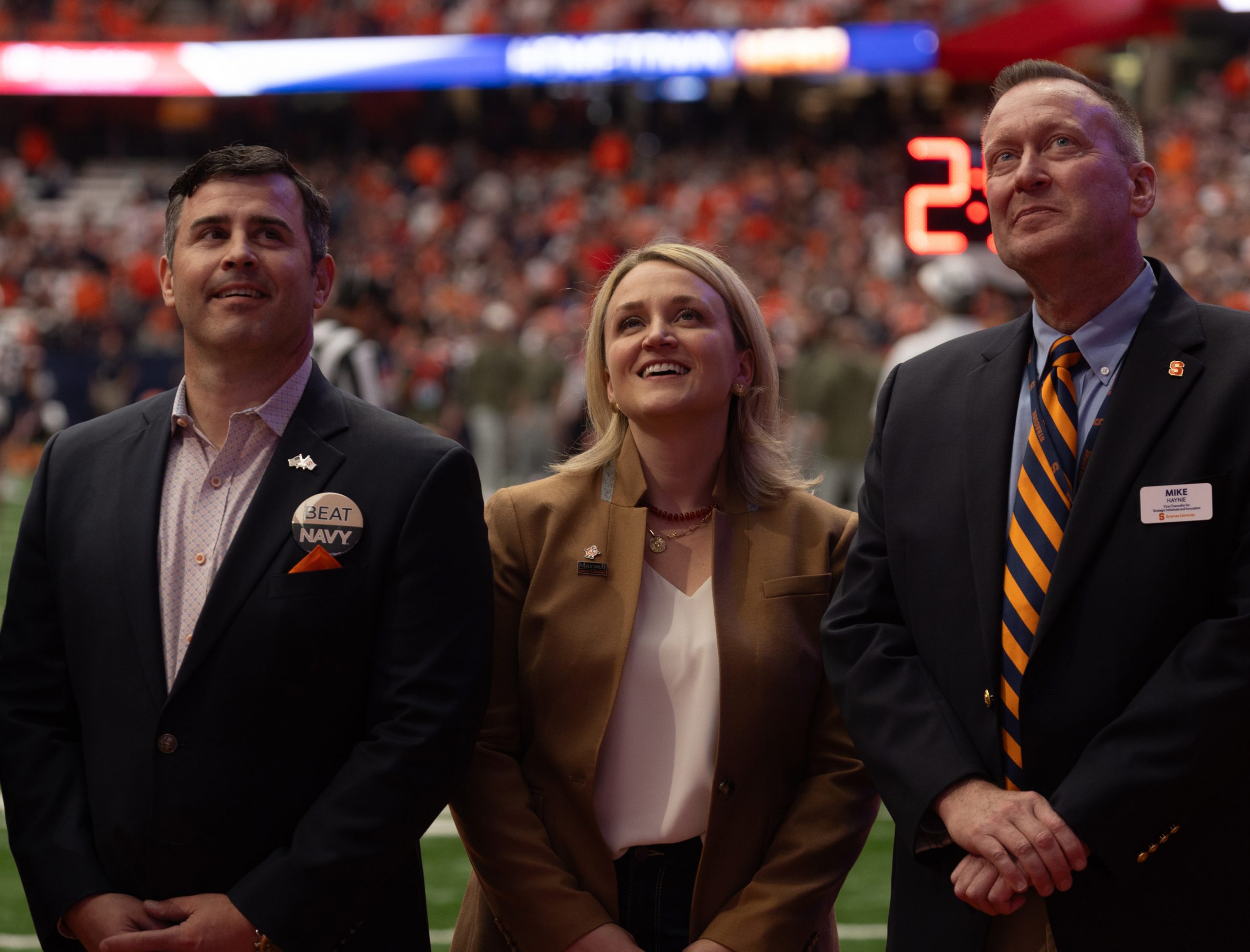 Three people standing next to one another on the field in the Dome during a game all looking up.