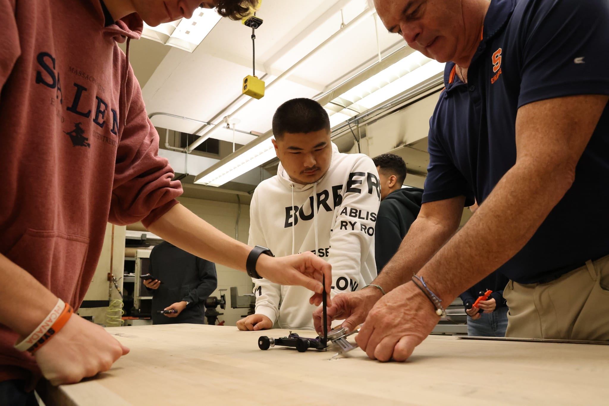 Three people standing at a table, with two of them working on a mini race-car. 