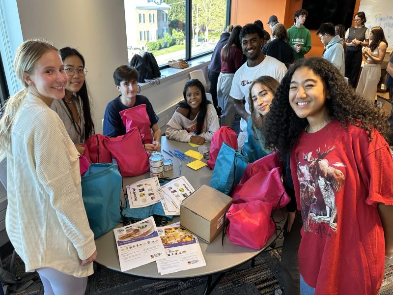 smiling college students along with young elementary students and the meal boxes they prepared and donated.