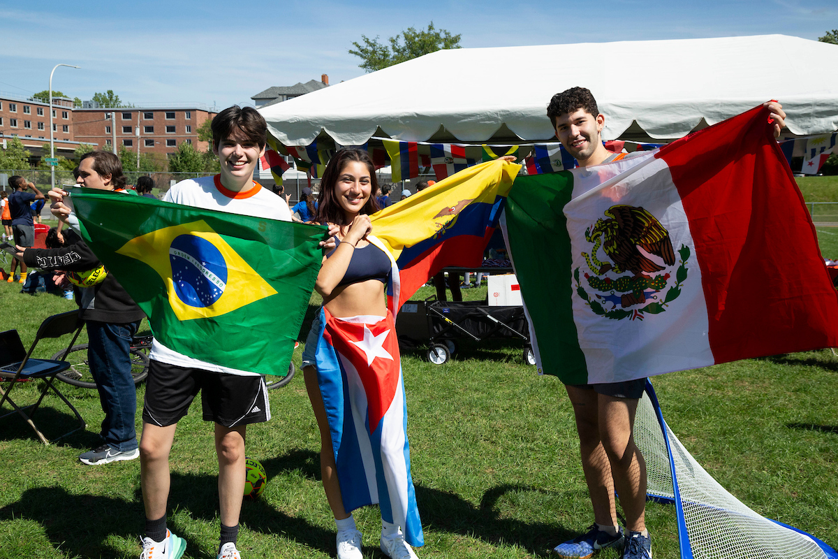 Three students standing together holding flags from different countries.