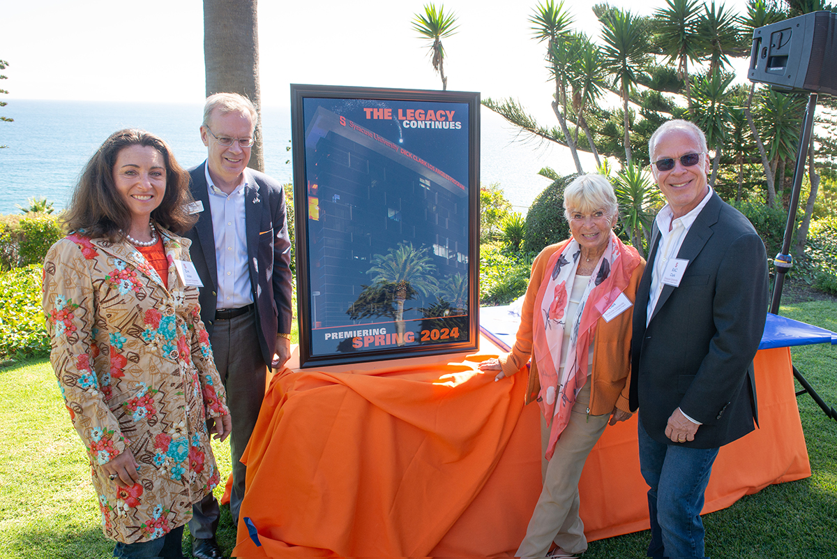 four people standing outside next to a table with a photo of a building