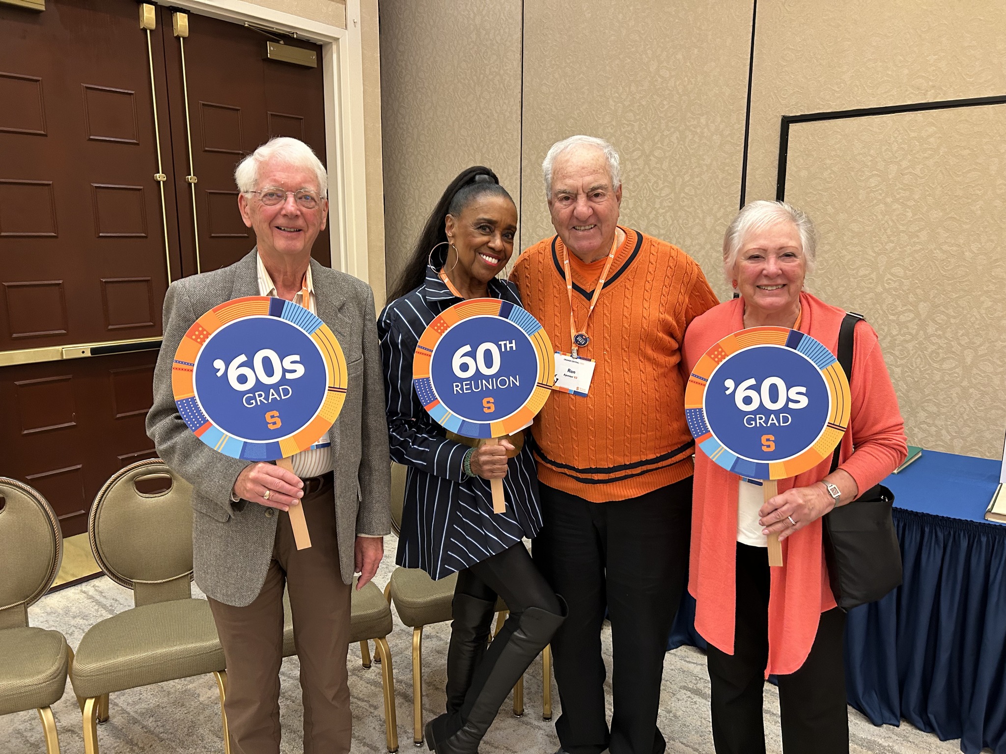 four people standing holding signs that represent their college class
