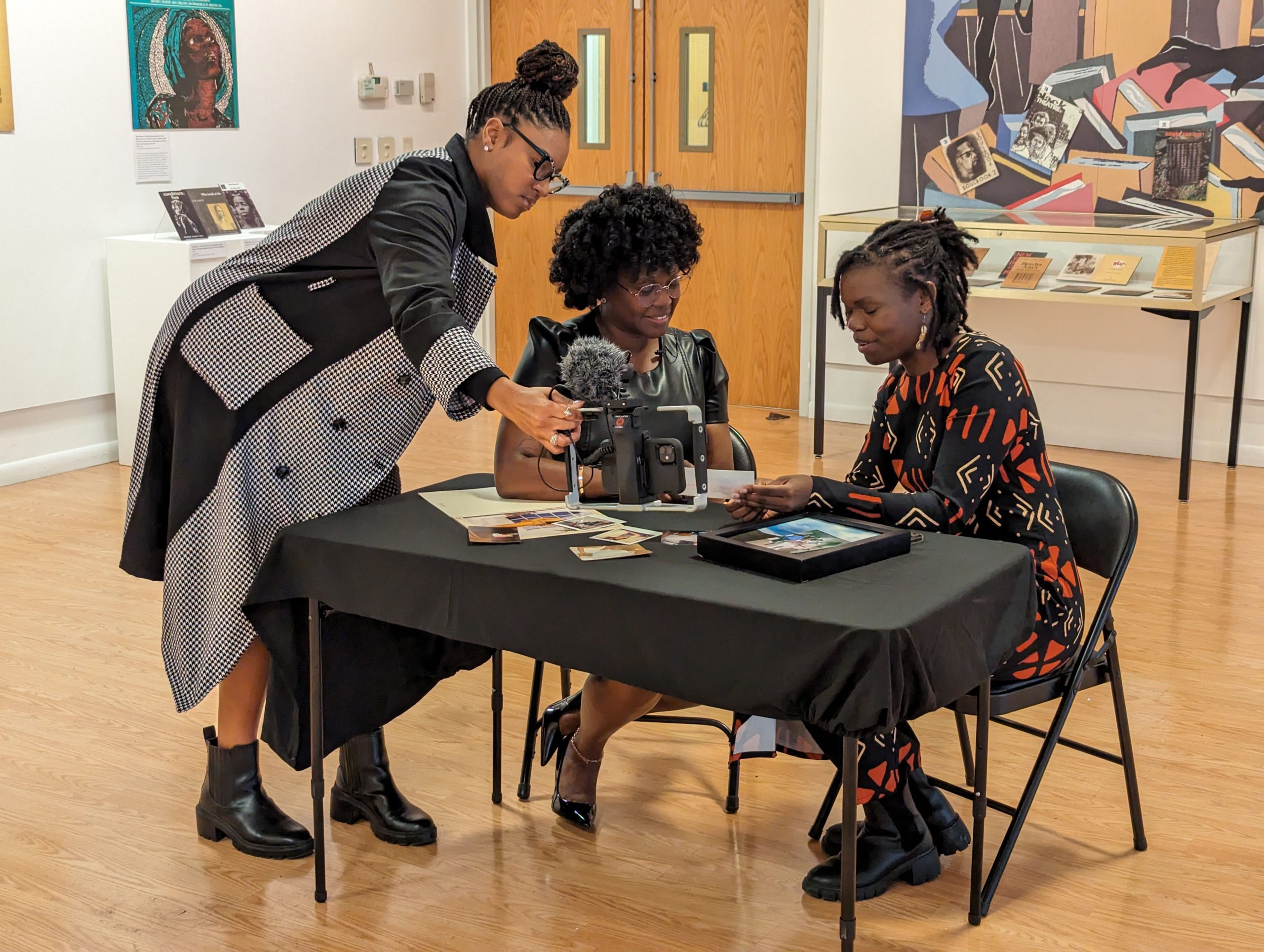 Two people sitting at a table and another one leaning over while they all look at a camera.