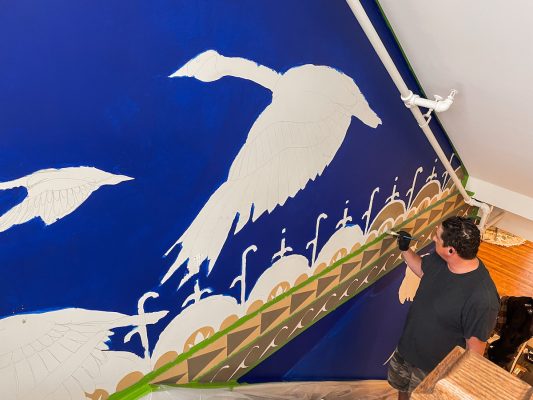 Individual painting a mural on a wall.