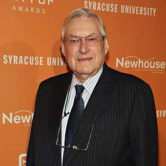 A man poses for a photo indoors with the words Syracuse University, Newhouse, and Mirror Awards in the backdrop.