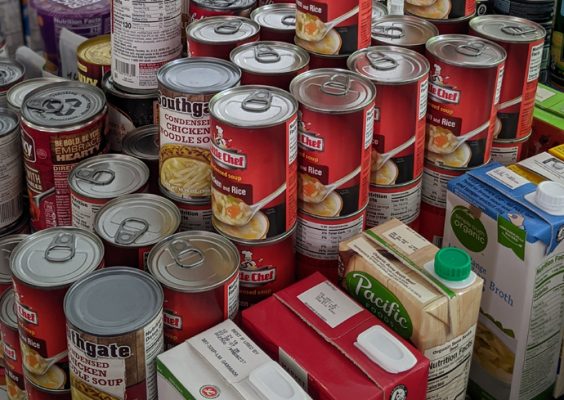 Cans of soup and other canned goods stacked on a shelf.