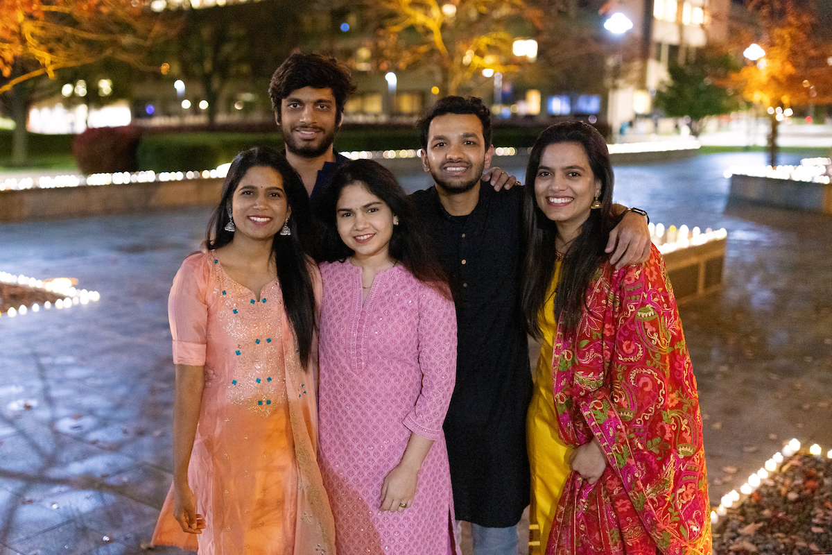 Students standing together at night on the Orange Grove which is lit up with small candles for Diwali.