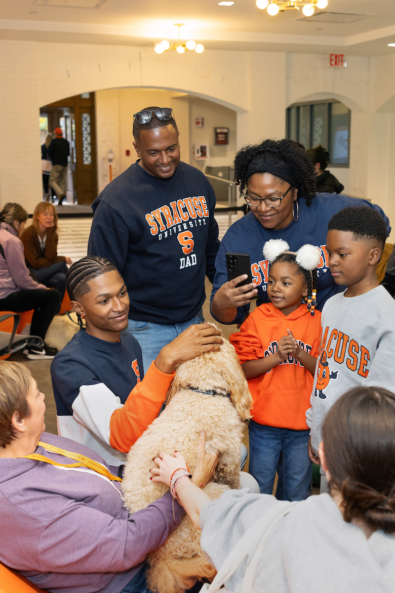 Group of people all wearing Syracuse gear petting a dog.
