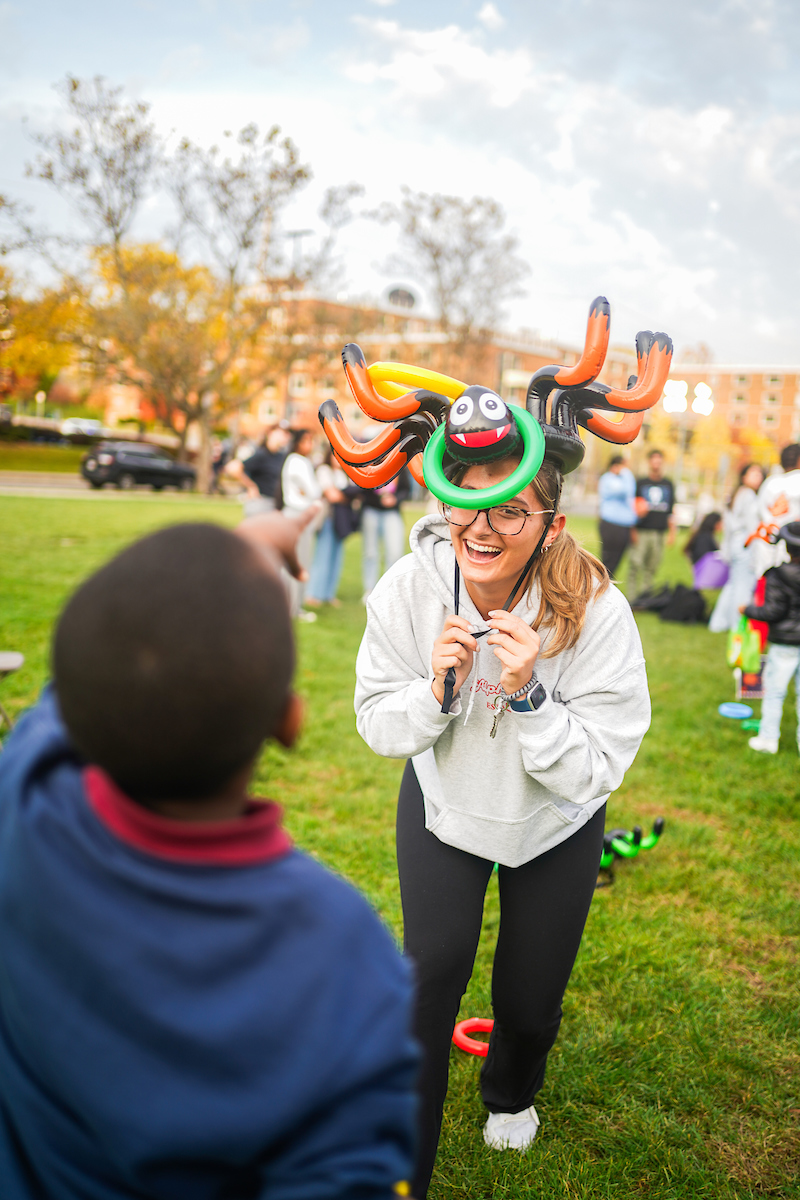 Student wearing a Halloween mask engaging with a child.