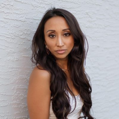 A woman poses for a headshot outdoors while standing against a white wall.