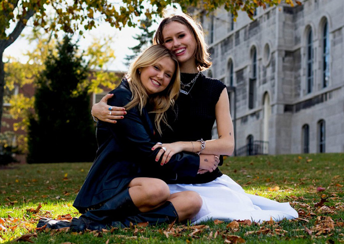 Moody Mag founders Emma Lueders and Jennie Bull hugging seated outdoors on campus