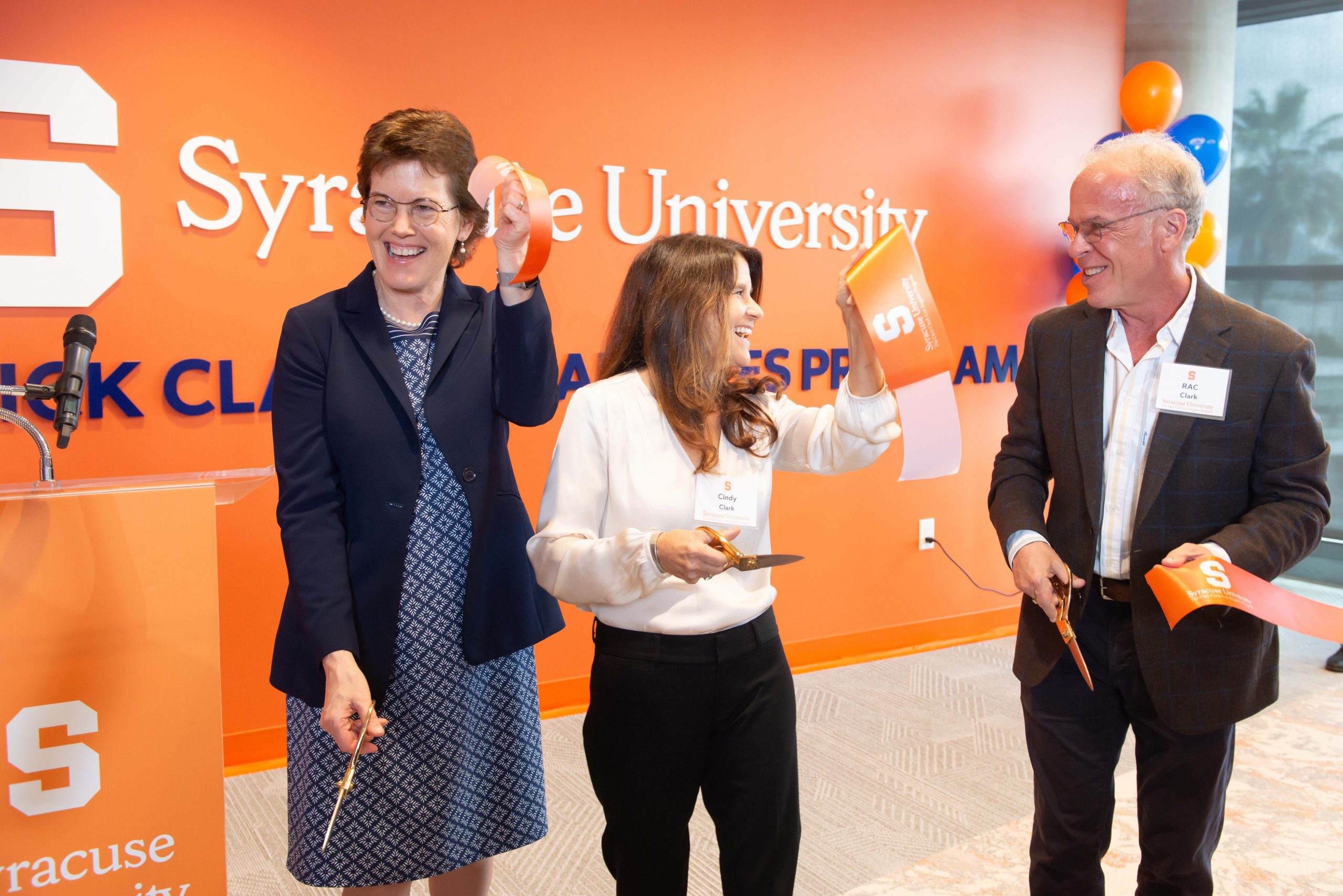 Three people standing together holding up ribbons they just cut during a ribbon cutting ceremony.