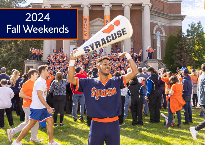 2024 Fall Weekends. Cheerleader standing on the Quad in front of Hendricks Chapel on game day with the band and spectators in the background.