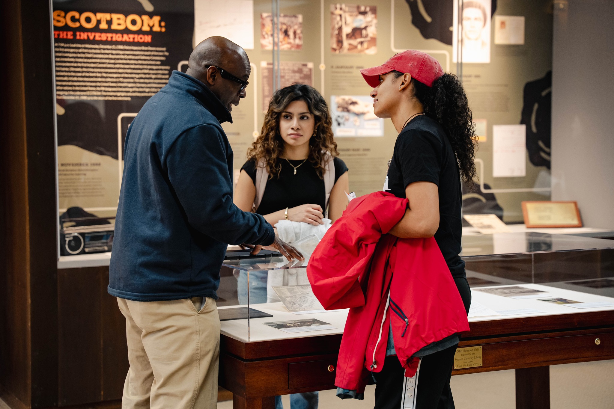 Three people standing in the library at a display talking. 