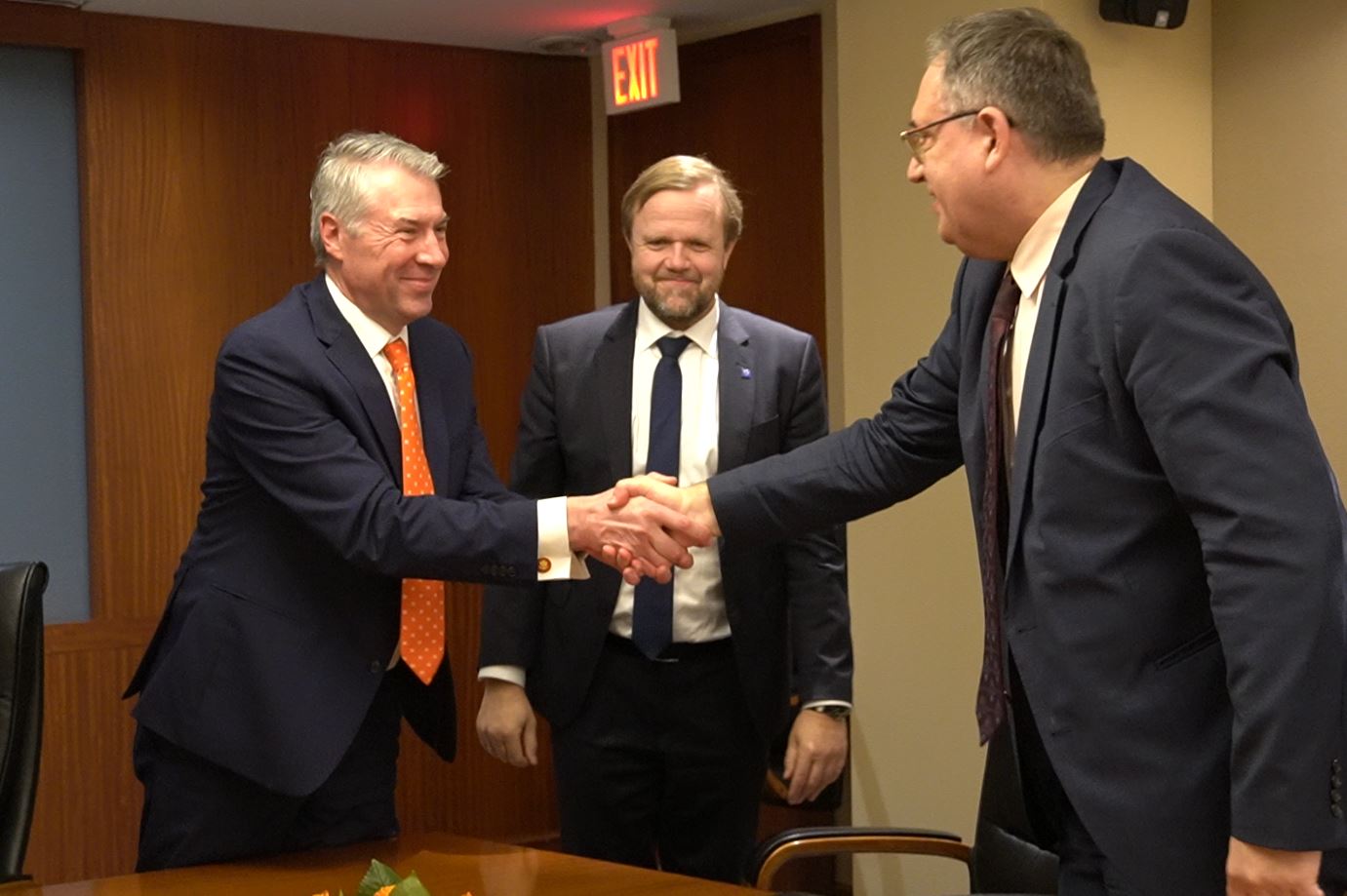 two people shaking hands in front of another person at conference table