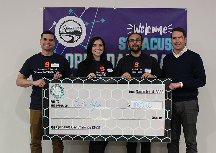 four people holding a display check in front of a banner