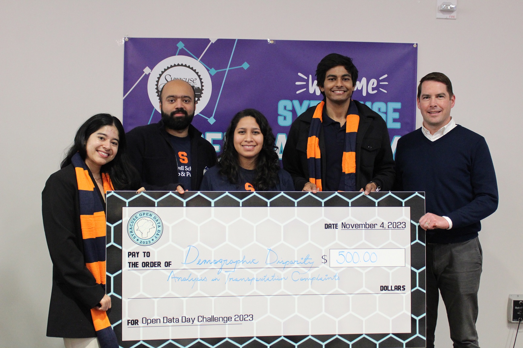 five people holding a display check in front of a banner